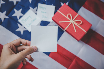 Obraz premium Christmas and New Year's Day, Close up holding hand note pad with message and Red gift box and ribbon with flag of the united states in the background.