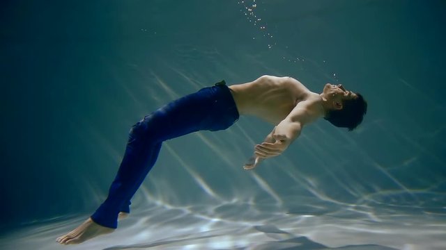 slow motion. a man unconscious under water floats to the surface