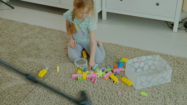 mom and daughter, a young woman cleans up with a vacuum cleaner, a little girl with blond hair collects toys, the designer in a container, helps mom