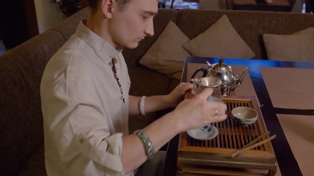Tea master preparing chinese tea on brewing table while traditional tea ceremony. Potter man pouring tea infusion from gaiwan to fairness pitcher glass pot with sieve. Traditional ceremony