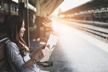 Asian woman tourist backpacker smiling and book to travel during the holidays.She is reading book waiting for the train to park the platform.