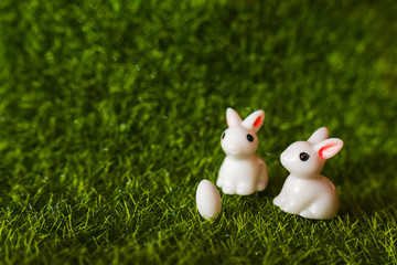 two figures of a rabbit and an egg on the grass.