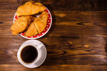 Cup of dark coffee and croissants on wooden table. Top view