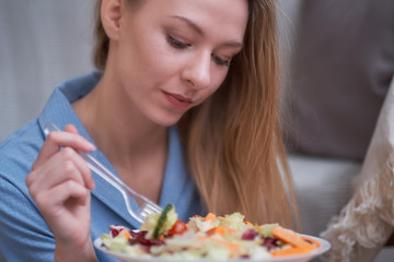 Obraz na płótnie Canvas young woman is eating salad at home, diet concept. disgruntled person, depression from having to diet, lack of fat in the diet.