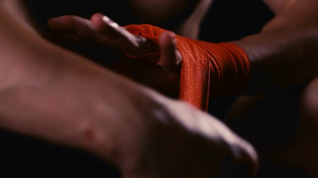 Male boxer wraps his hands with red handwrap before the fight training, 4k slow motion