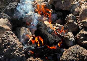 Hot bright bonfire at stones on sunny day. Burning logs. Glow flame