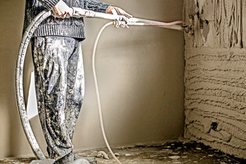 Worker applying gypsum plaster to the aerated concrete wall with a spray plastering machine.  Internal finishing in procces - obrazy, fototapety, plakaty