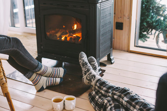 Cold fall or winter day. People drinking tea and resting by the stove. Closeup photo of human feet in warm woolen socks over fire place. Hygge concept of cozy winter weekend in cabin.