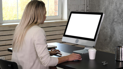 Business woman in dress sitting on workplace near the window and using computer in office. White Display.