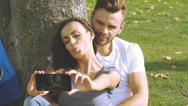 Happy couple taking a picture of themselves with a smartphone on a green lawn. Slow motion.