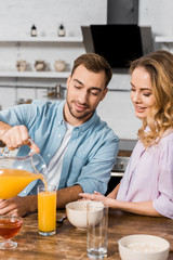 smiling man pouring orange juice in glass for pretty wife
