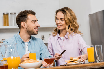 pretty woman holding knife and toast and looking at handsome husband at table