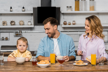 smiling parents looking at cute boy sitting at kitchen table