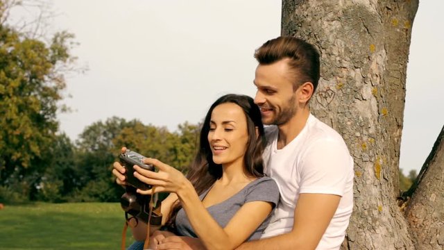 Happy couple taking a picture of themselves with an old camera on a green lawn.