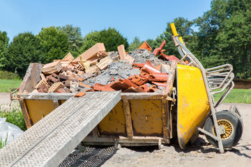 Container with debris and wheelbarrow outside