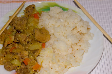 Curry with rice in a white plate and food sticks on a bamboo napkin
