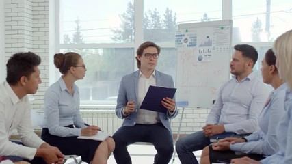 Zoom in of male business coach explaining financial diagram on clipboard to company employees during educational seminar