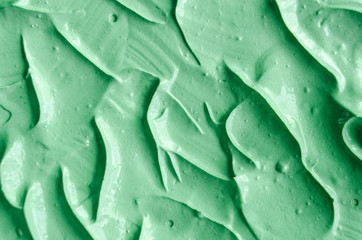 Green cosmetic clay (facial mask, cream, body scrub) texture close up, selective focus. Abstract background with brush strokes.
