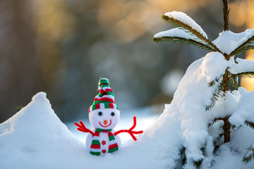 Small funny toy baby snowman in knitted hat and scarf in deep snow outdoors on bright blue and...
