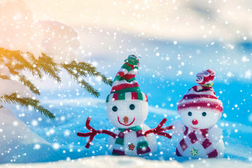 Fototapeta premium Two small funny toys baby snowman in knitted hats and scarves in deep snow outdoors on bright blue and white copy space background. Happy New Year and Merry Christmas greeting card.