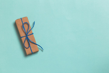 Wrapped gift box with blue ribbon on turquoise background with copy space. Top view