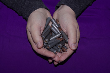 Female hands stretching a handful of cartridges from a Kalashnikov assault rifle on a purple background close-up