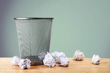 Trash can with paper sheets on wooden table