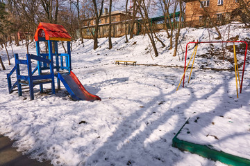 empty bright playground with broken parts and without a swing on the street in winter on a frosty day with snow