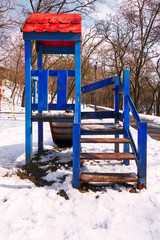 empty bright playground with broken parts and without a swing on the street in winter on a frosty day with snow