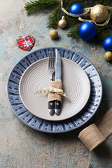 Christmas table setting on decor background. Blue and gray plate, cutlery, festive decorations.