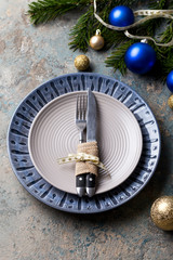 Christmas table setting on decor background. Blue and gray plate, cutlery, festive decorations.
