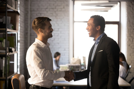 Diverse smiling businessmen shake hands getting acquainted introducing make first impression, happy friendly african and caucasian workers handshaking talking greeting, welcoming new employee concept - Powered by Adobe
