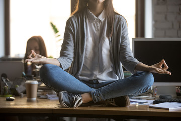 Young woman office worker student sitting on desk in lotus position doing yoga exercise for balance...
