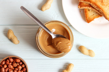  creamy peanut butter in a glass jar and peanuts beans on wooden background top view