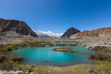 Fototapeta na wymiar Panorama shot of small turquoise mountain lake under the sunny day with blue sky along Karakorum Highway in Passu, Hunza district of Pakistan.
