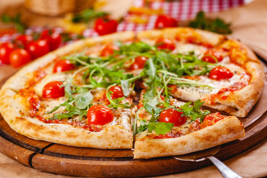 Italian Pizza with tomatoes, mozzarella cheese and arugula on wooden cutting board. Close up