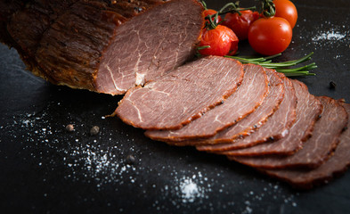 Roast beef sliced with cherry tomatoes and spices on a black stone board