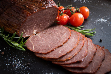 Roast beef sliced with cherry tomatoes and spices on a black stone board