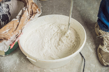 Young male painter kneads putty with water in a bucket using a hand-held mixer for building mixes