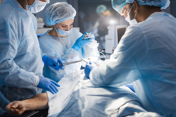 Attentive medical workers operating their patient. A surgery like this requires an anesthesiologist, a general surgeon to remove tumor and, at least two surgical nurses. - obrazy, fototapety, plakaty
