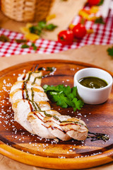 Sliced grilled chicken breast with pesto sauce on wooden cutting board. Close up