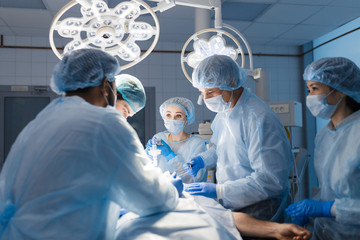 Multiracial Team of Surgeons concentrating on a patient during a heart surgery at a hospital. Mature caucasian doctor sharing his experiences with multiethnic colleagues.