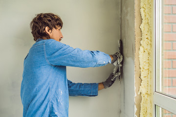 master is applying white putty on a wall and smearing by putty knife in a room of renovating house...