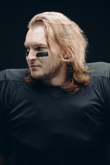 Portrait of determined caucasian blonde American football sportsman in black uniform with painted...