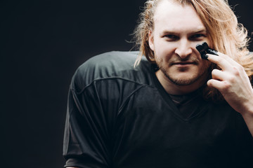 Young caucasian blonde man in american football player's ammunition wearing black painted stripes...