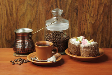 Cup of coffee, coffee pot, coffee grinder, cakes, sugar on a wooden table