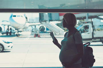 Pregnant woman is traveling by plane standing near the window