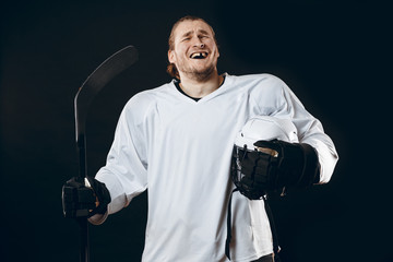 Obraz premium Portrait of cheerful proud caucasian hockey player smiling with teeth, looking in camera with happy and relaxed face expression, posing after victory in hockey match with stick, isolated on white