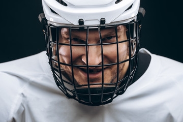 Portrait of hockey keeper in protective helmet with carbonic defence in white uniform grinning at...