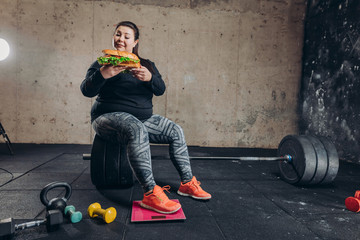 obese woman combining sport and junk food, fat girl having snack during workout. full length photo....